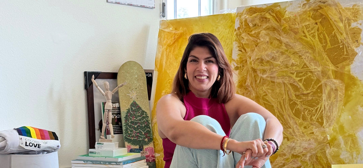 Aakriti sitting in her studio surrounded by paintings and art supplies, smiling